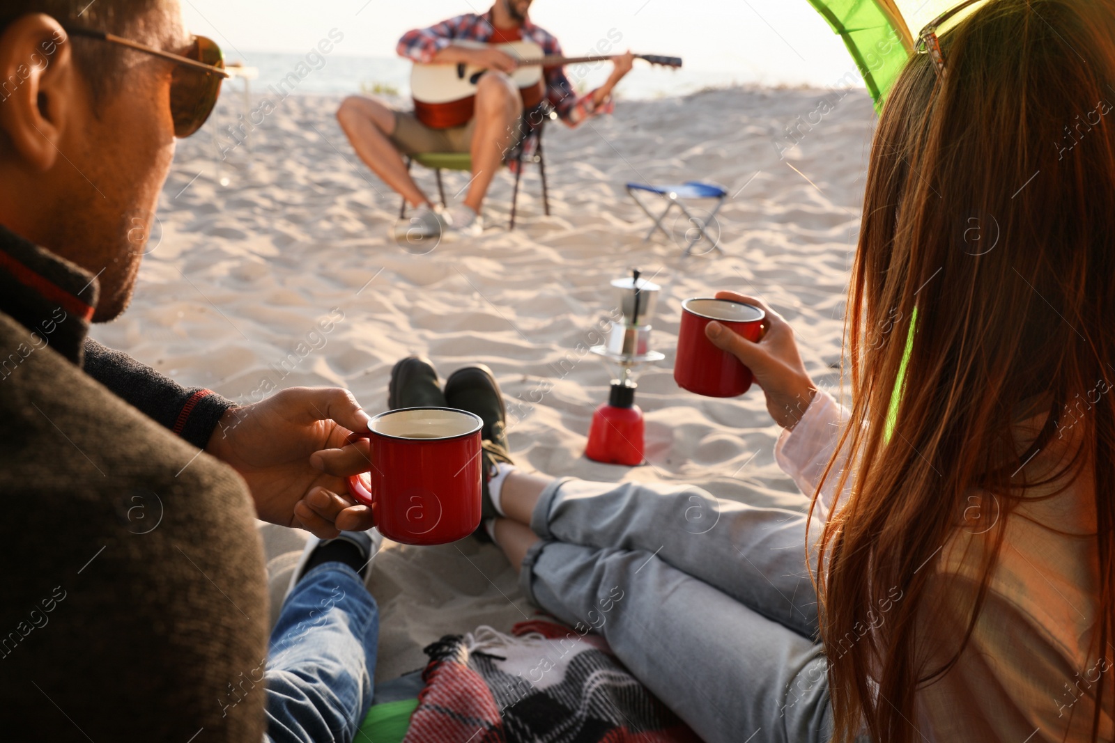 Photo of Friends resting on sandy beach. View from camping tent