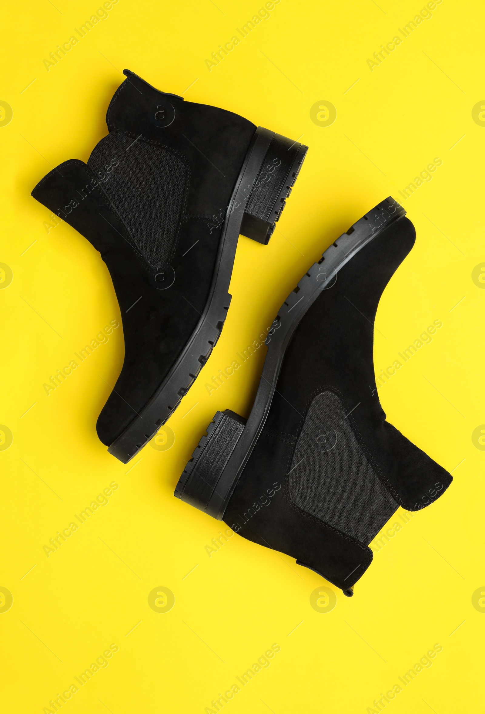 Photo of Stylish black female boots on yellow background, flat lay