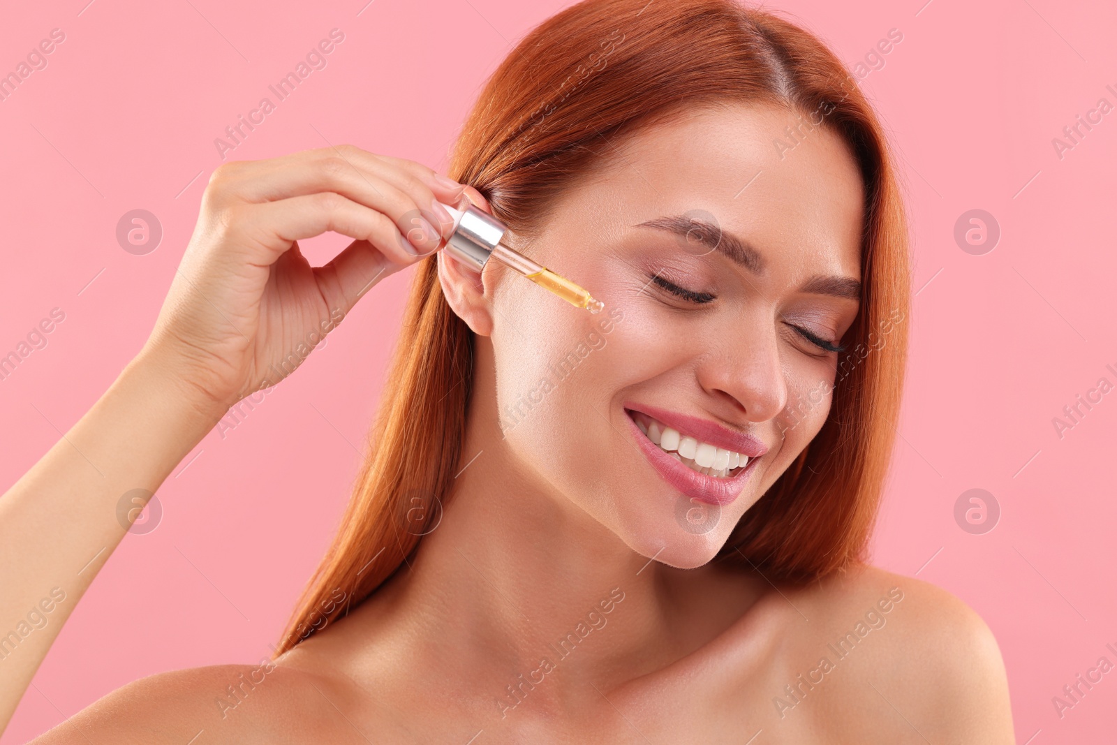 Photo of Beautiful young woman applying cosmetic serum onto her face on pink background