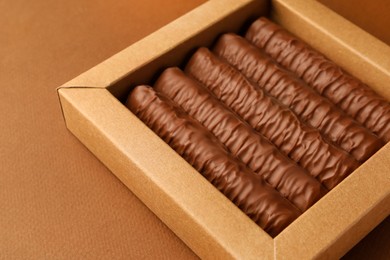 Photo of Sweet tasty chocolate bars in box on brown background, closeup