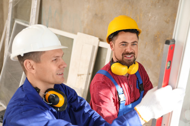 Workers using bubble level for installing window indoors