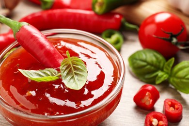 Photo of Spicy chili sauce with basil on table, closeup