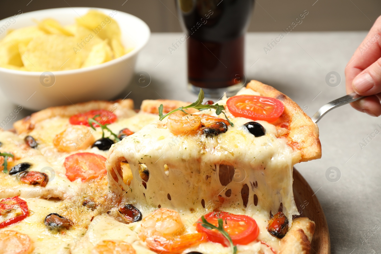 Photo of Woman taking slice of cheese pizza with seafood at table, closeup