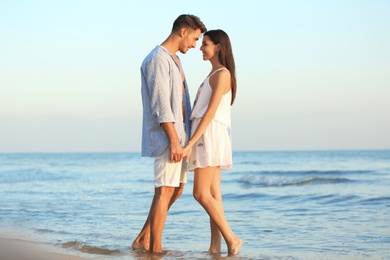 Happy young couple holding hands at beach on sunny day