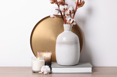 Photo of Burning candles, book and vase with cotton branches on wooden table against white background