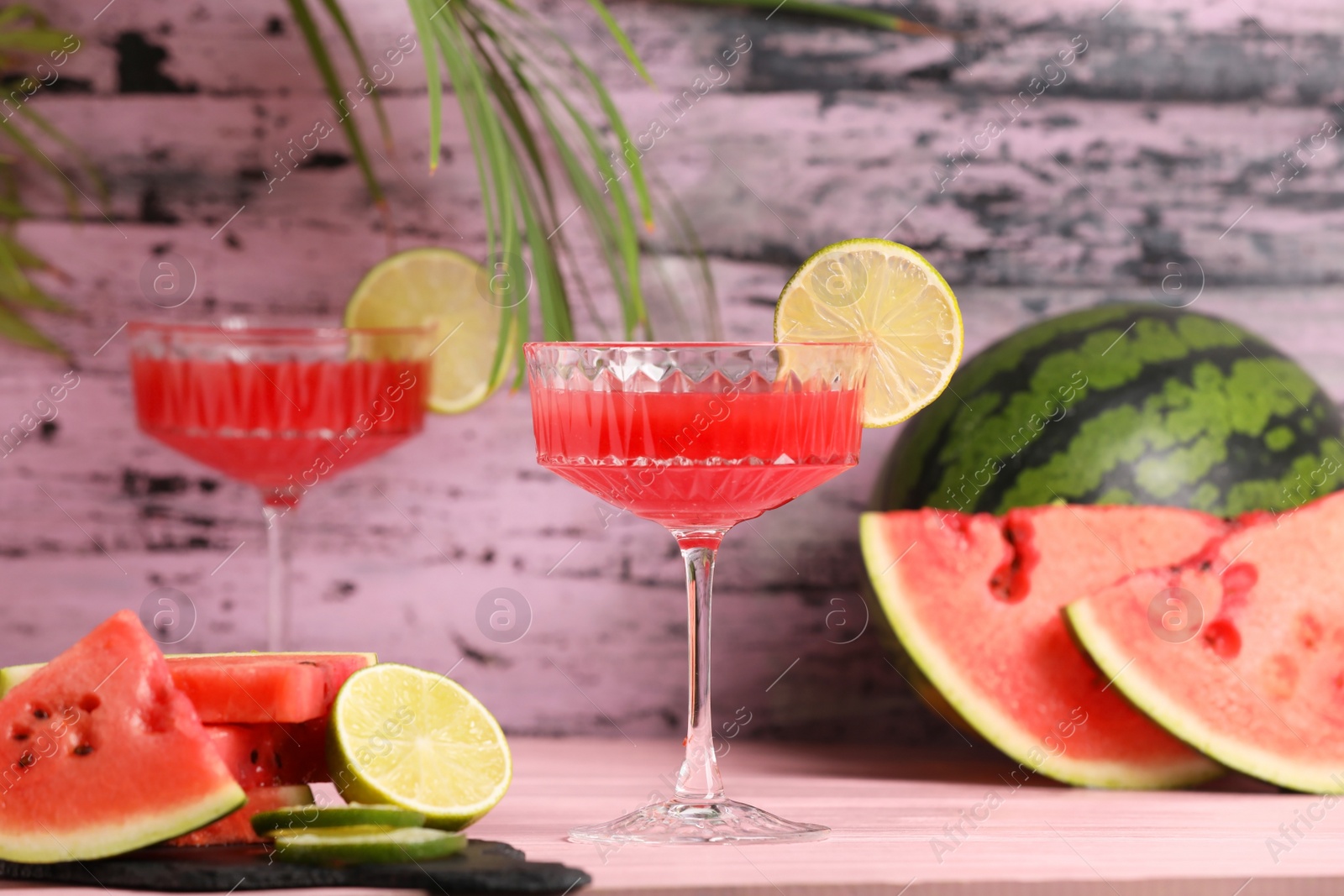 Photo of Cocktail glass of delicious fresh watermelon juice with lime on light wooden table