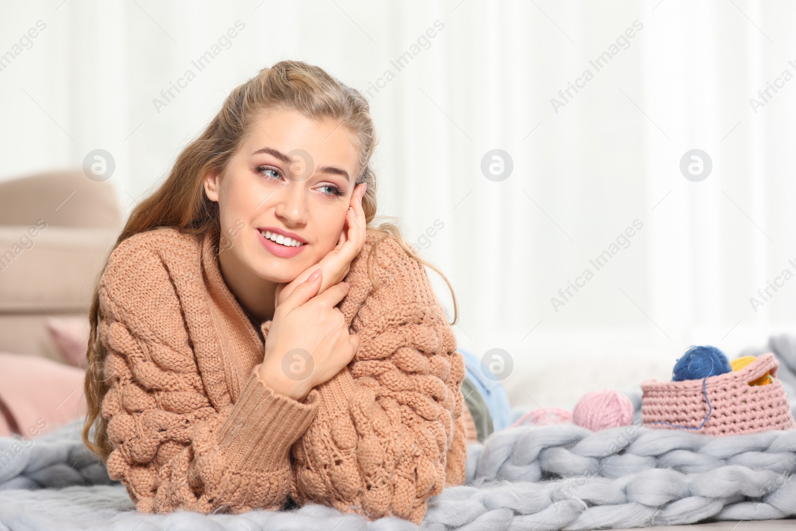 Photo of Attractive smiling young woman in cozy warm sweater lying on floor at home. Space for text