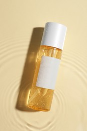 Photo of Bottle of cosmetic oil in water on beige background, top view
