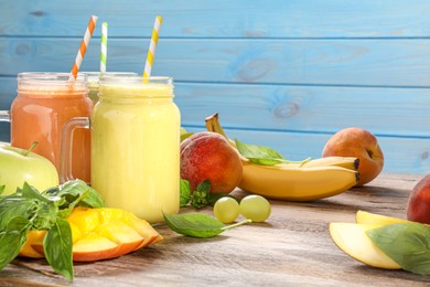 Photo of Mason jars of different tasty smoothies and fresh ingredients on wooden table. Space for text