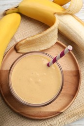 Glass of tasty banana smoothie with straw and fresh fruits on white wooden table, flat lay