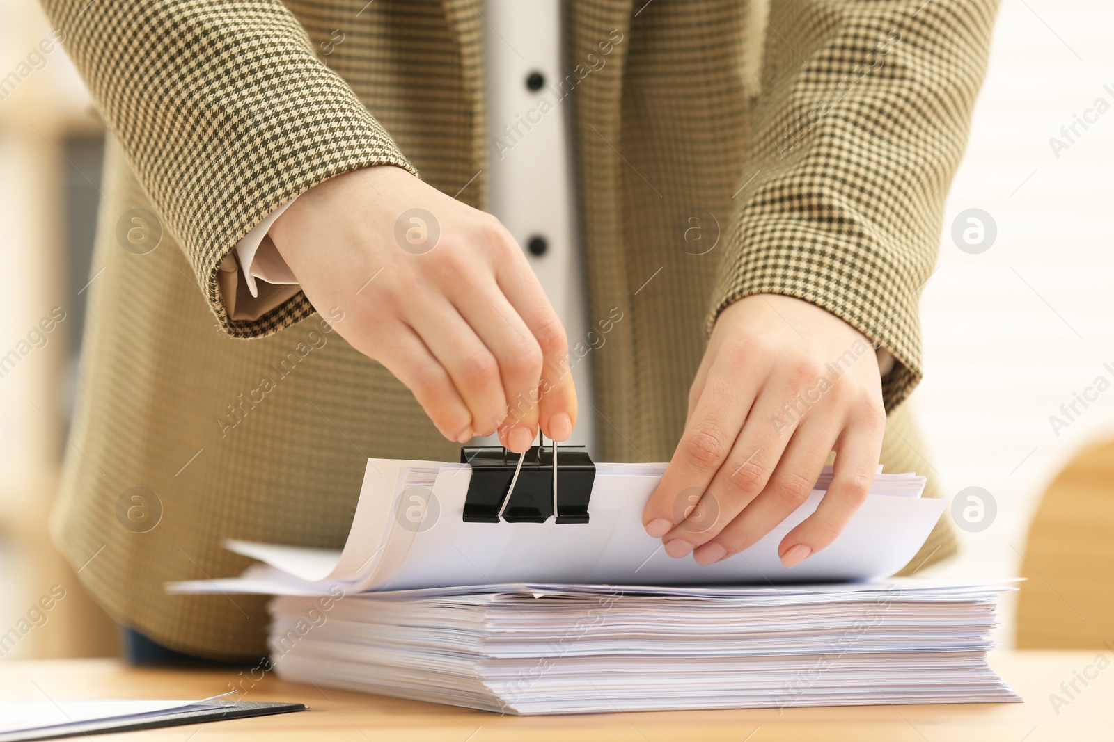 Photo of Woman attaching documents with metal binder clip at table in office, closeup