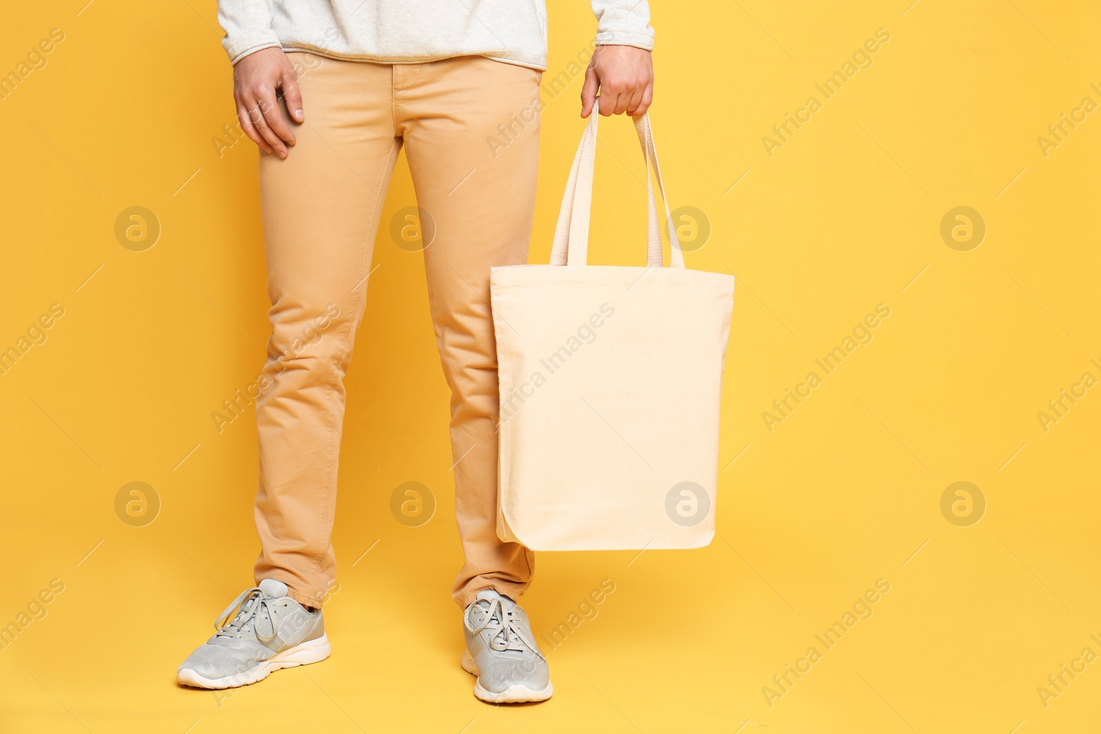 Photo of Young man with eco bag on yellow background, closeup. Space for text