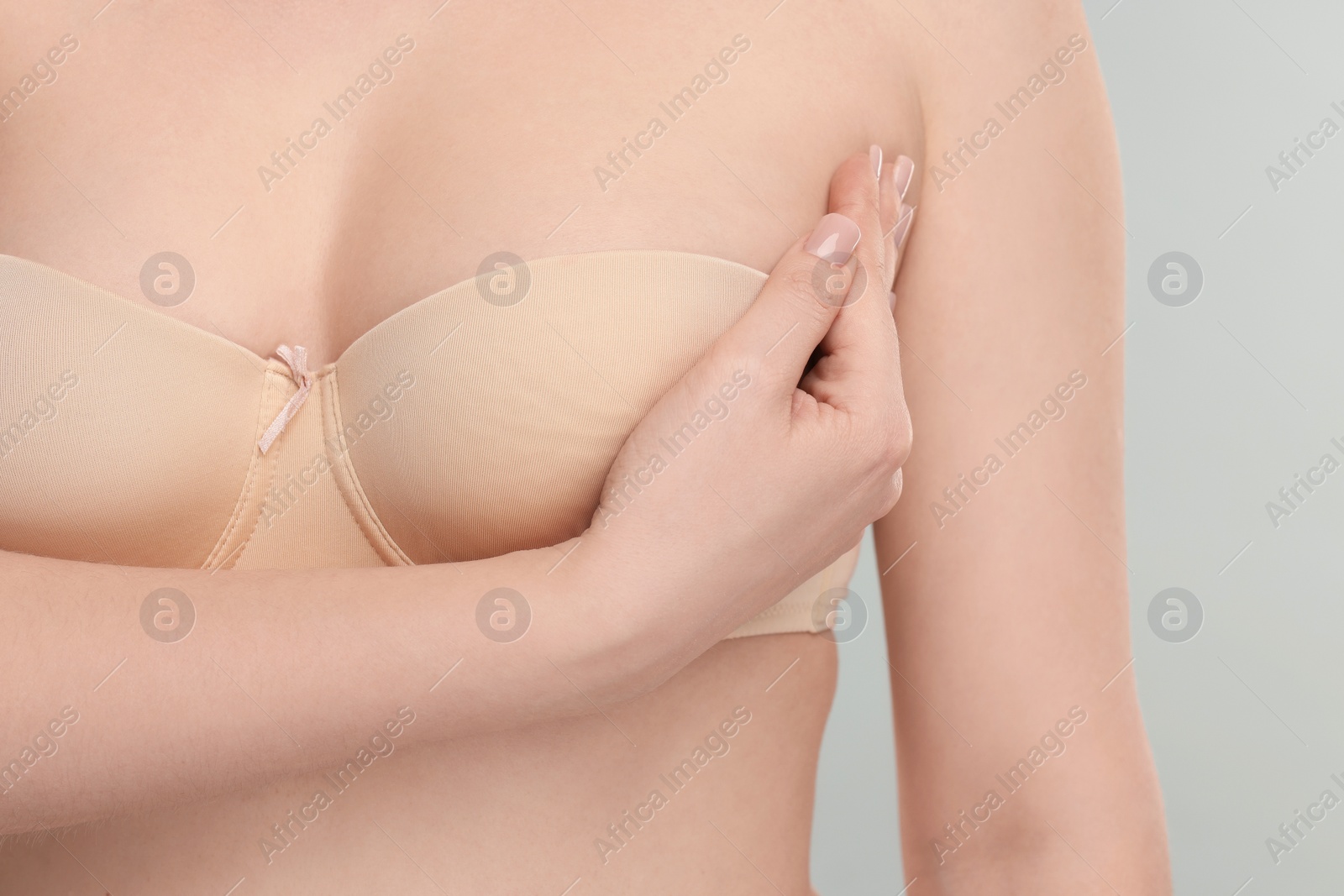 Photo of Mammology. Young woman doing breast self-examination on light grey background, closeup