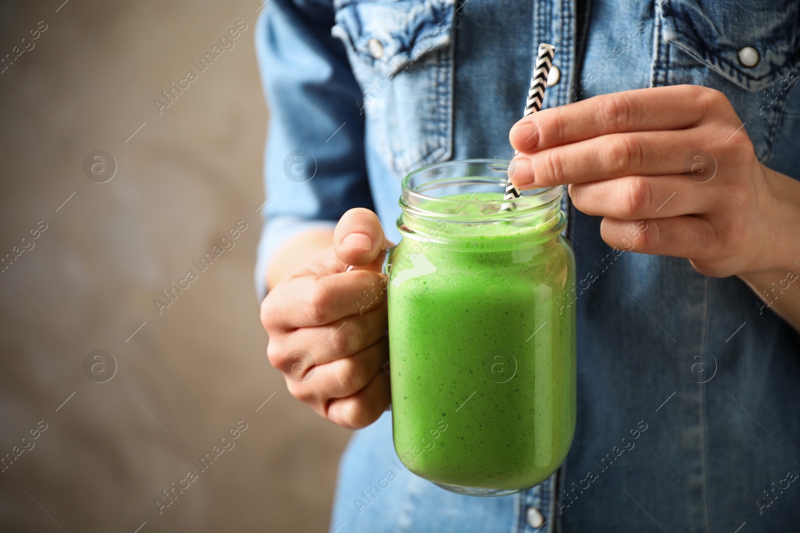 Photo of Woman holding tasty kale smoothie on brown background, closeup