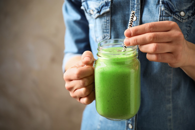 Photo of Woman holding tasty kale smoothie on brown background, closeup