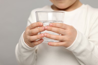 Little girl holding glass of fresh water on light grey background, closeup