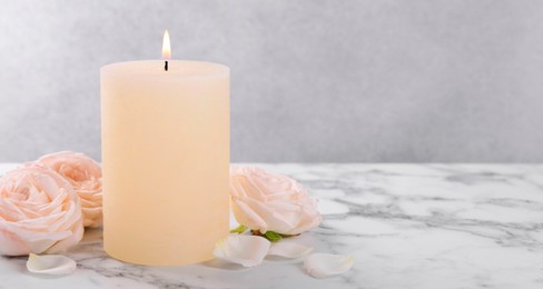 Spa composition with burning candle and flowers on white marble table, space for text