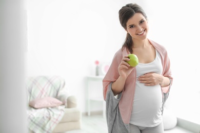 Young pregnant woman holding apple at home