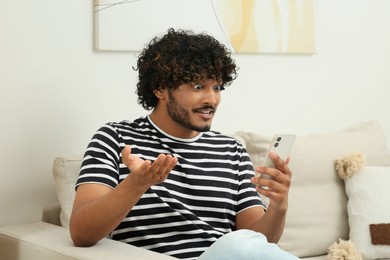 Photo of Handsome smiling man having video call via smartphone in room