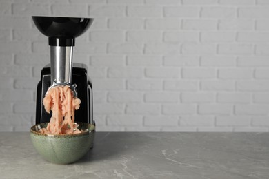 Electric meat grinder with chicken mince on grey marble table near white wall. Space for text