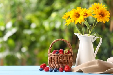 Photo of Wicker basket with different fresh ripe berries and beautiful flowers on light blue table outdoors, space for text