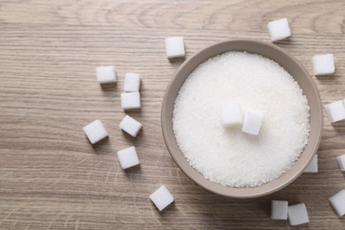 Photo of Different types of white sugar in bowl on wooden table, top view. Space for text