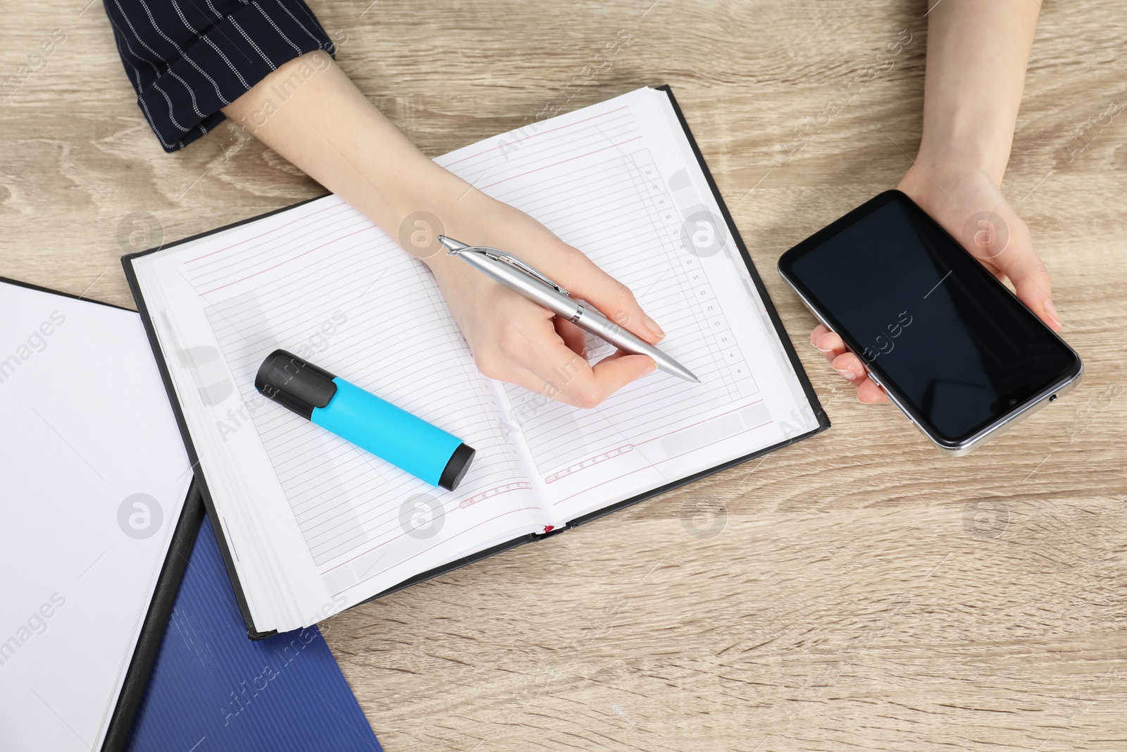 Photo of Woman taking notes while using smartphone at wooden table, top view