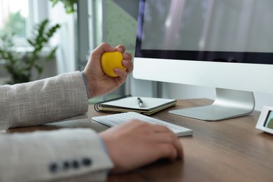 Photo of Man squeezing antistress ball while working with computer in office, closeup