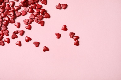 Red heart shaped sprinkles on pink background, flat lay