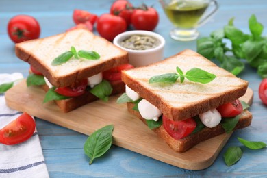 Photo of Delicious Caprese sandwiches with mozzarella, tomatoes, basil and pesto sauce on light blue wooden table