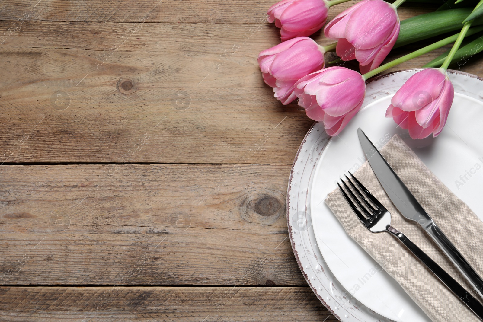 Photo of Stylish table setting with cutlery and tulips on wooden background, flat lay. Space for text