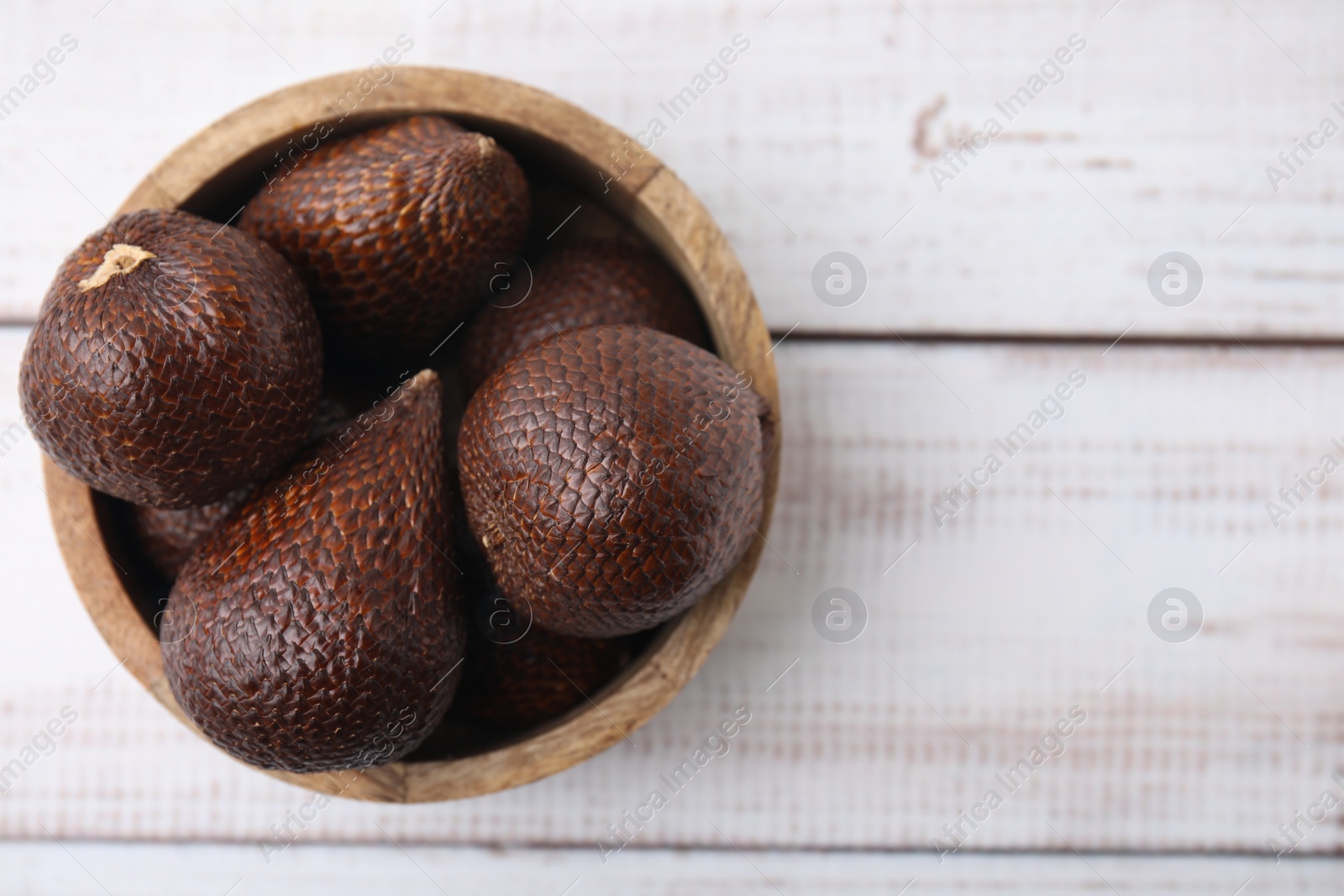 Photo of Fresh salak fruits in bowl on white wooden table, top view. Space for text