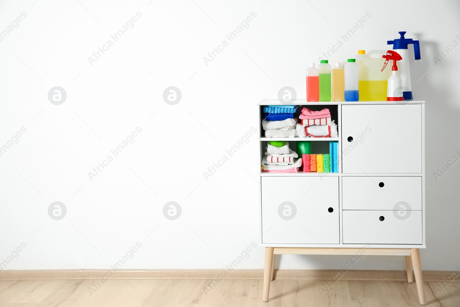 Photo of Cabinet with different cleaning supplies near white wall. Space for text