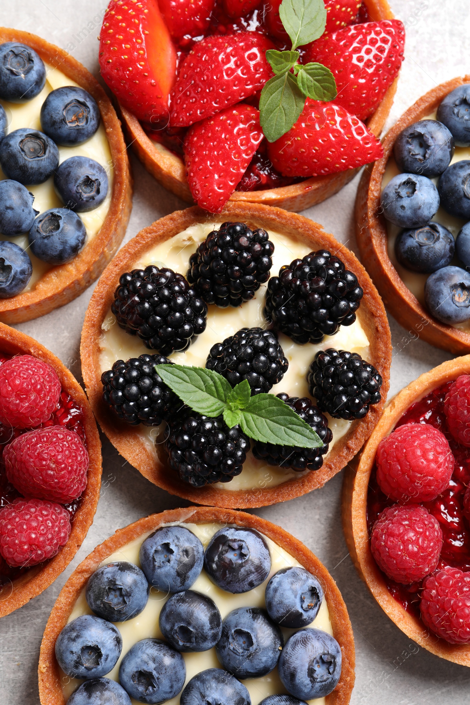 Photo of Tartlets with different fresh berries on light table, flat lay. Delicious dessert