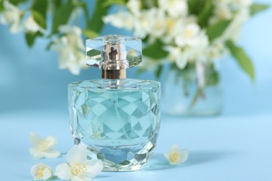 Photo of Aromatic perfume in bottle and beautiful jasmine flowers on light blue background, closeup