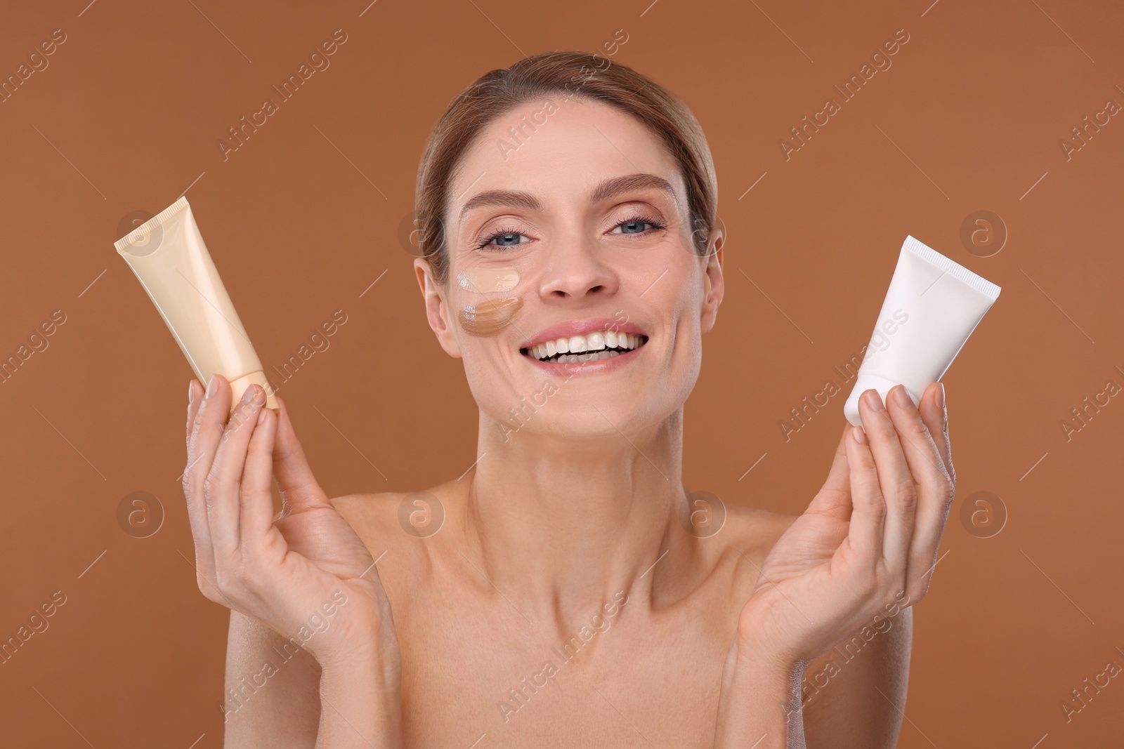 Photo of Woman holding tubes of foundation on brown background