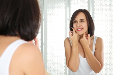 Happy mature woman with clean skin looking at mirror in bathroom