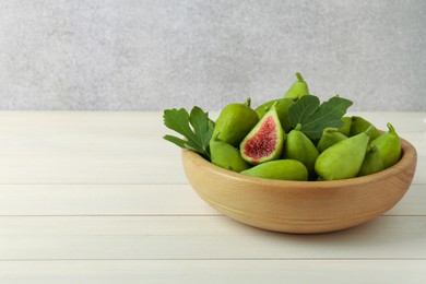 Cut and whole fresh green figs on white wooden table near grey wall, space for text