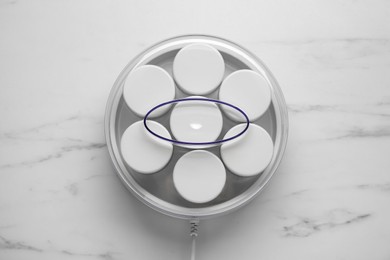 Modern yogurt maker with jars on white marble table, top view