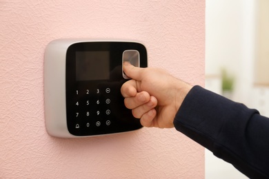 Photo of Man scanning fingerprint on alarm system at home, closeup