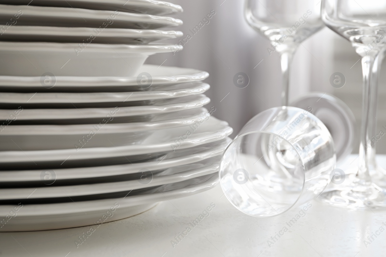 Photo of Stacked plates and glasses on white table, closeup