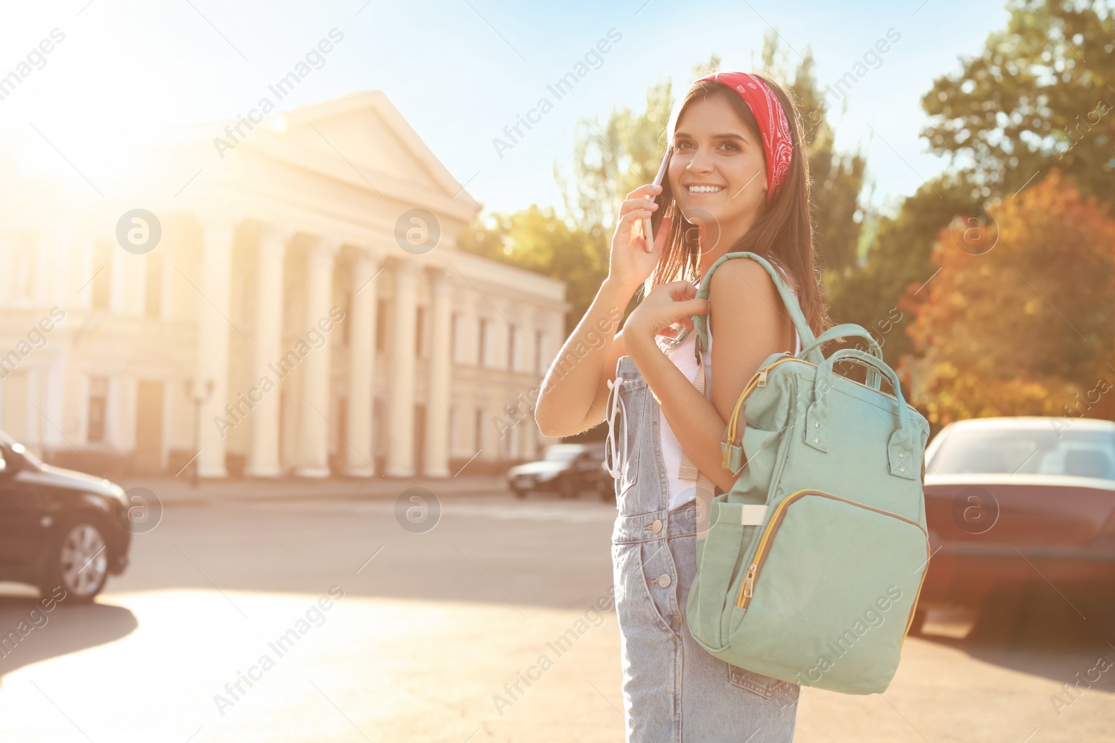 Photo of Young woman with stylish turquoise bag talking on phone outdoors