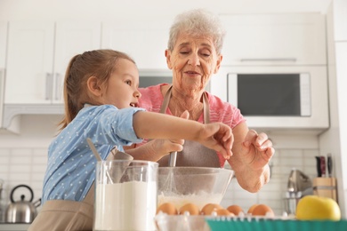 Photo of Cute girl and her grandmother cooking in kitchen