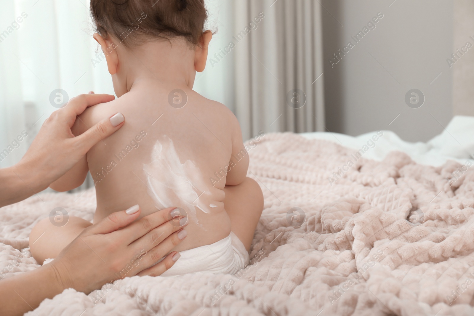 Photo of Mother applying body cream on her baby indoors, space for text