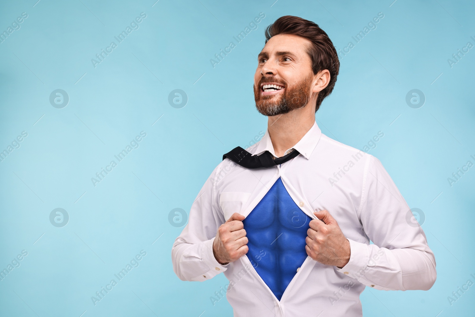 Image of Happy businessman wearing superhero costume under suit on light blue background. Space for text