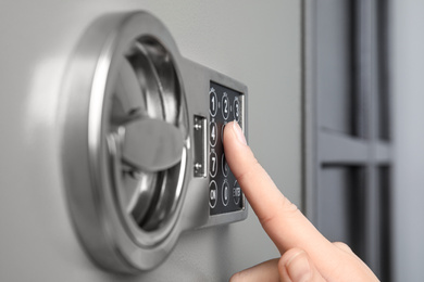 Photo of Woman opening steel safe with electronic lock, closeup
