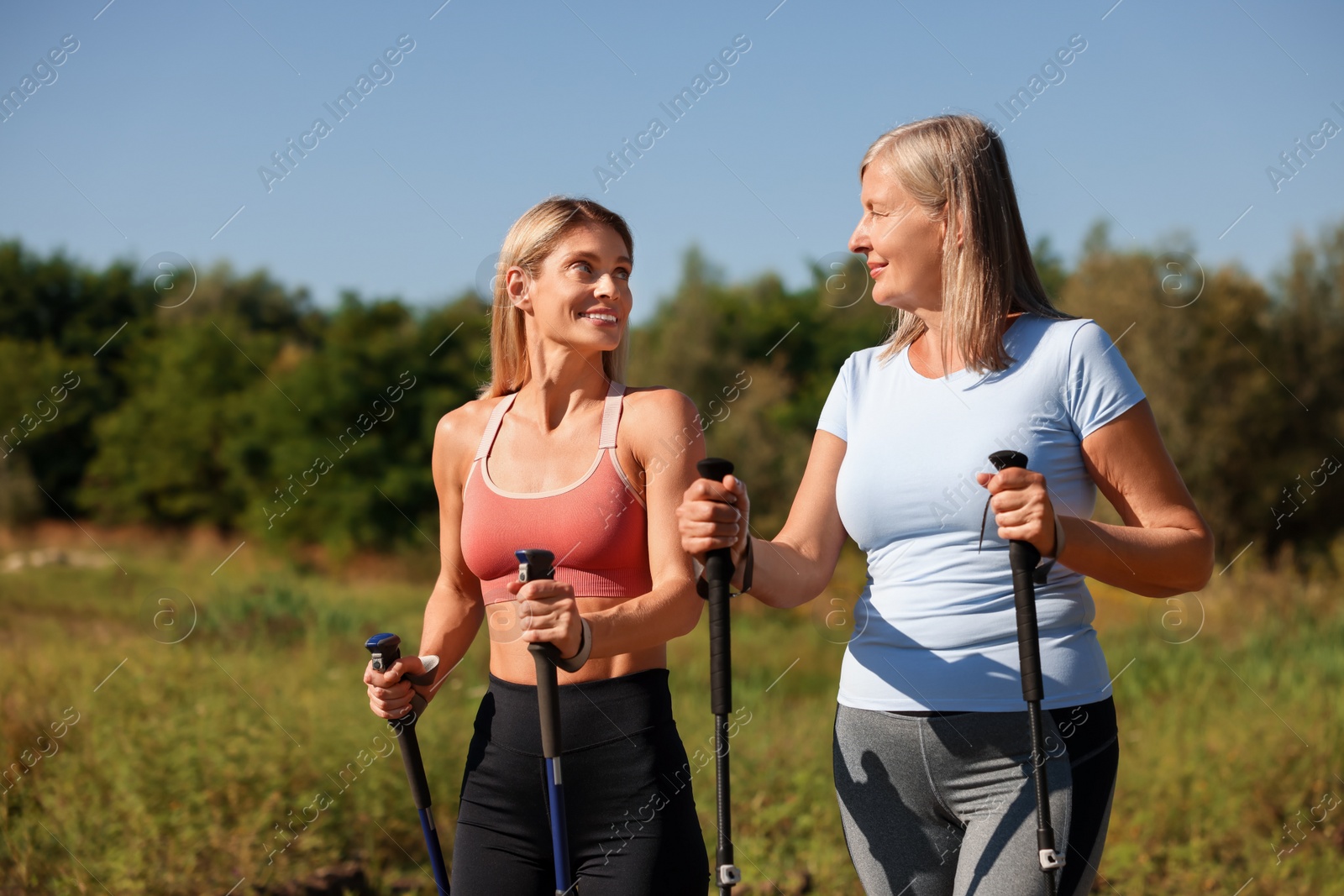 Photo of Happy women practicing Nordic walking with poles outdoors on sunny day