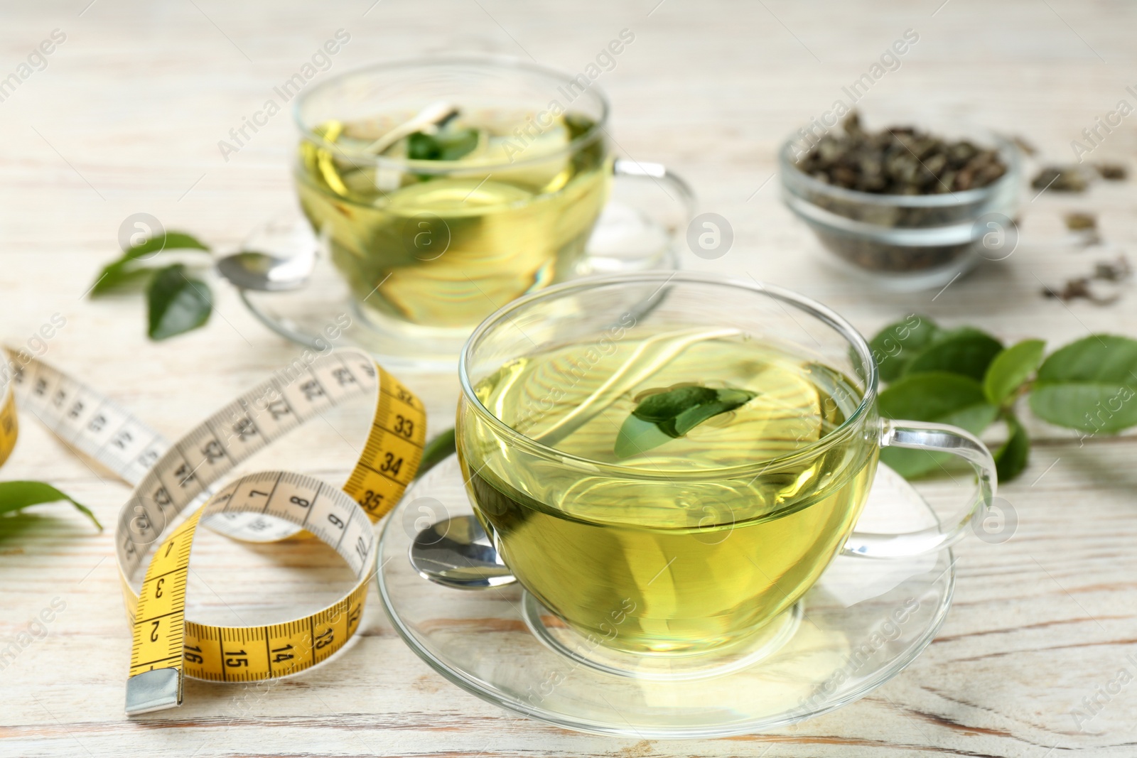 Photo of Diet herbal tea with green leaf and measuring tape on white wooden table