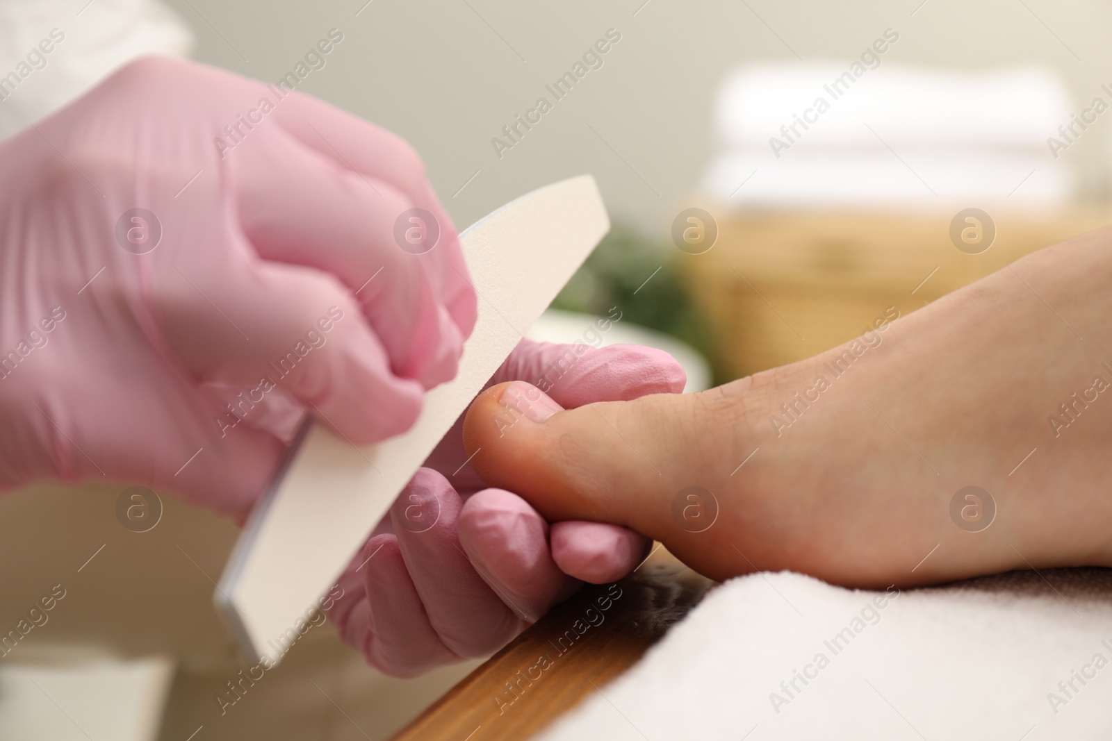 Photo of Professional pedicurist filing client`s toenails in beauty salon, closeup