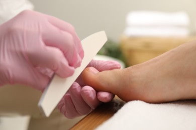 Photo of Professional pedicurist filing client`s toenails in beauty salon, closeup